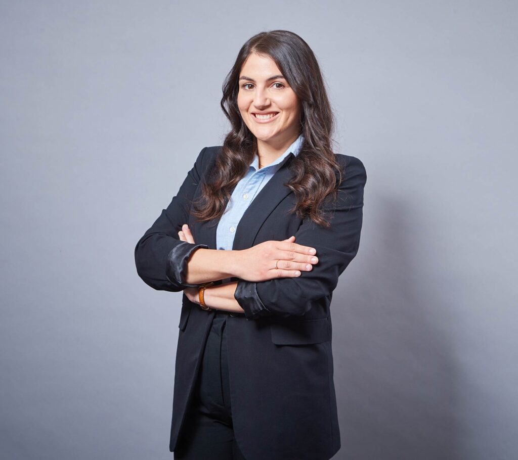 Das Portrait von Cangül Er in einem dunklen Hosenanzug und hellblauer Bluse. Sie hat dunkle, lange Haare.